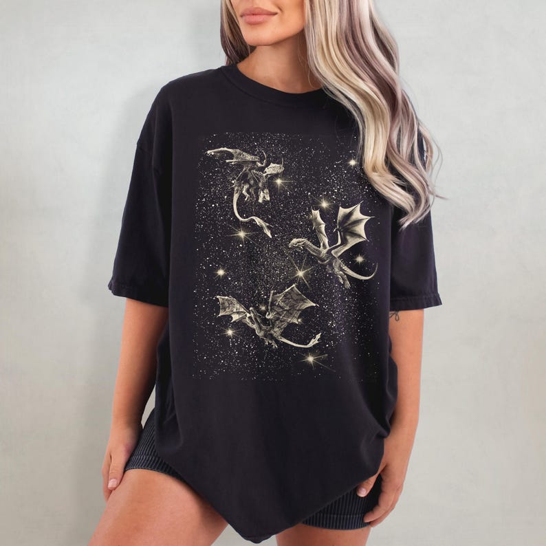 May include: Black oversized t-shirt with a graphic print of three gold dragons flying in a starry sky.