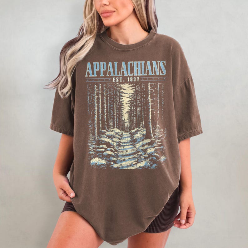 May include: A brown oversized t-shirt with a graphic print of a forest path and the text "Appalachians Est. 1937".