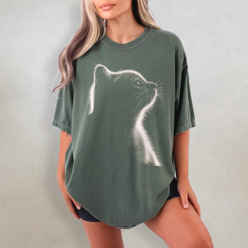May include: A green oversized t-shirt with a white silhouette of a cat's head looking to the right.