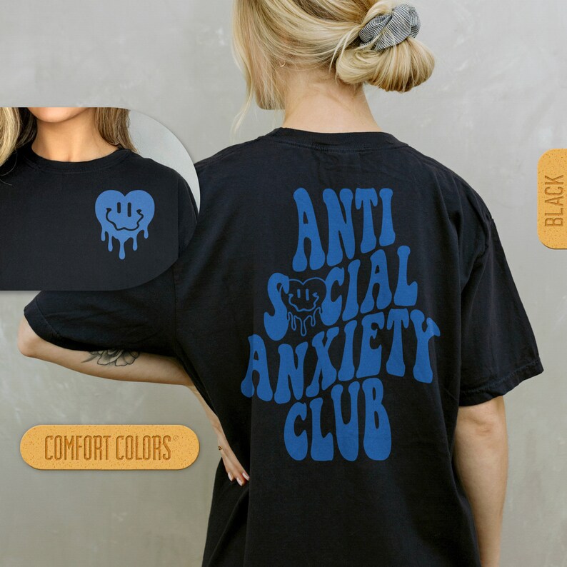 K&ouml;nnte beinhalten: Schwarzes T-Shirt mit blauem Text "Anti Social Anxiety Club" und einem blauen, tropfenden Smiley-Herz. Das Shirt wird an einem Model gezeigt.