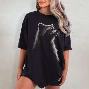 May include: A black oversized t-shirt featuring a white graphic of a raccoon's face. The raccoon is looking to the right.