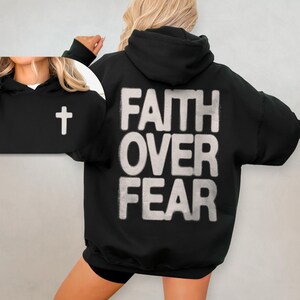 May include: Black hooded sweatshirt with the words "Faith Over Fear" printed in white on the back. A small white cross is visible on the left sleeve.