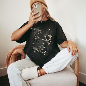 May include: A black t-shirt with a graphic print of three gold dragons flying in a starry sky.
