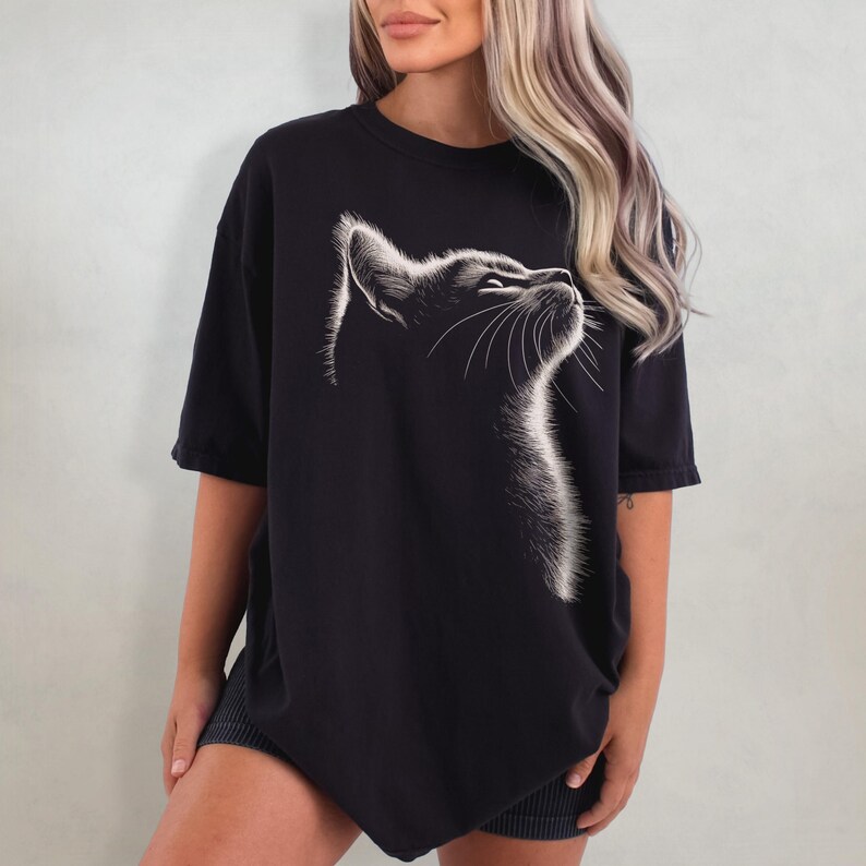 May include: A black oversized t-shirt featuring a white graphic of a cat's face looking upwards.
