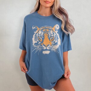 May include: A blue oversized t-shirt with a white tiger face graphic. The tiger has orange stripes.