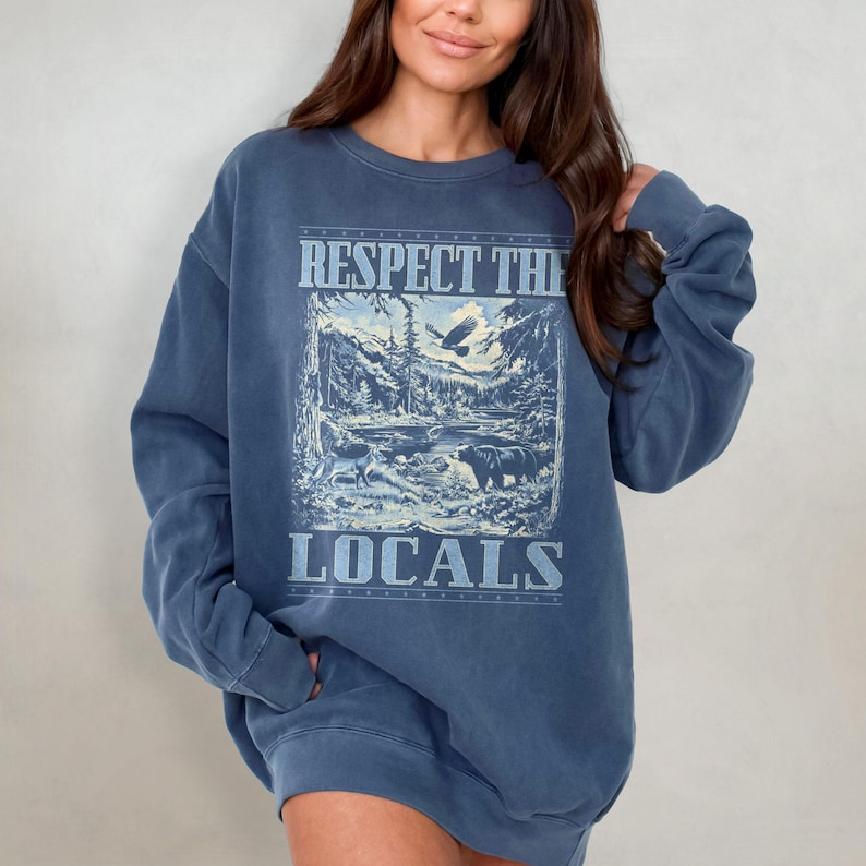 May include: A blue oversized sweatshirt with a graphic print of a mountain scene, an eagle, and the text "Respect the Locals".