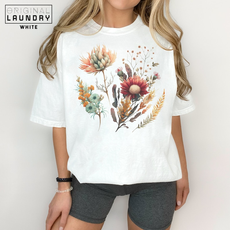 May include: White t-shirt with a floral print featuring a variety of flowers in shades of orange, red, and yellow.