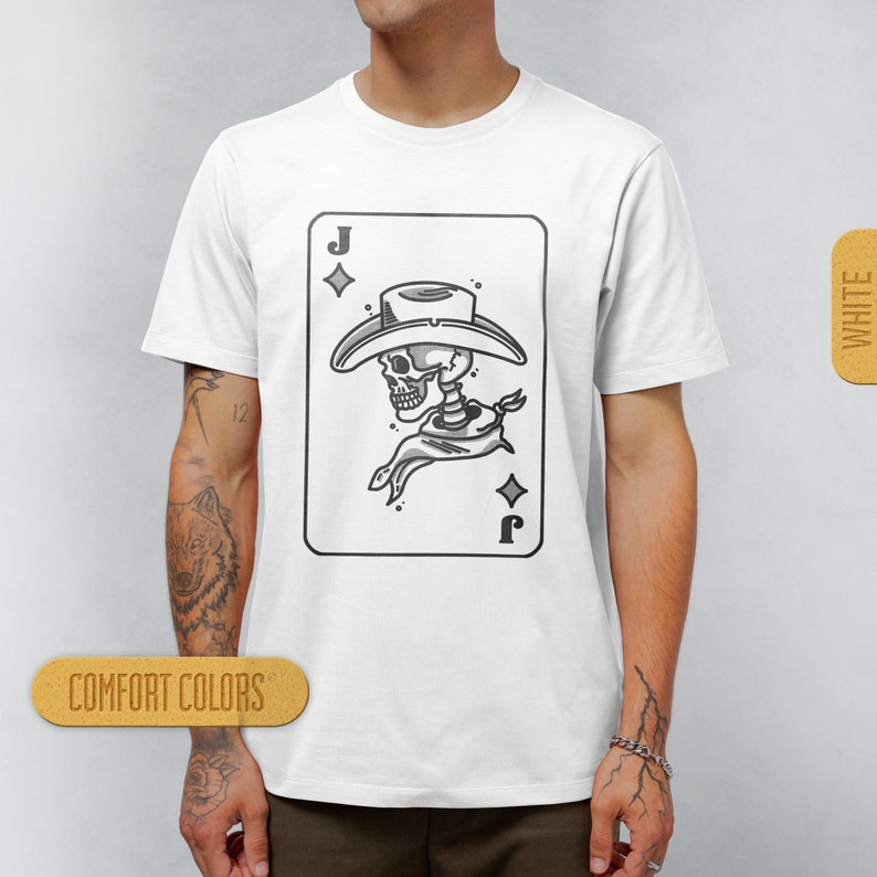 Puede incluir: Camiseta blanca con una ilustraci&oacute;n en blanco y negro de un esqueleto con un sombrero de vaquero y un pa&ntilde;uelo. La ilustraci&oacute;n tiene la forma de una carta de juego con la letra 'J' y un s&iacute;mbolo de diamante.
