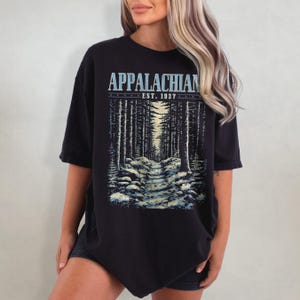 May include: Black oversized t-shirt with a graphic print of a forest path and the text "Appalachian Est. 1937".