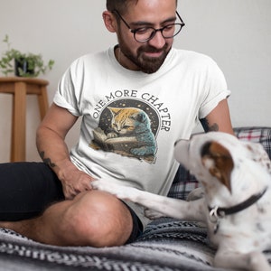 May include: A white t-shirt with a graphic of a cat reading a book with the text "One More Chapter" in a circle around the cat.