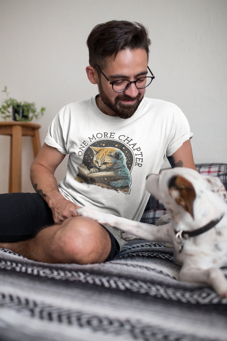 May include: A white t-shirt with a graphic of a cat reading a book with the text "One More Chapter" in a circle around the cat.
