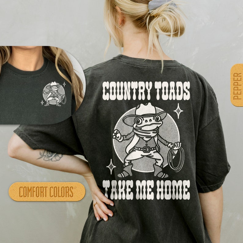 Puede incluir: Camiseta negra con un gr&aacute;fico blanco de una rana de dibujos animados con un sombrero de vaquero y sosteniendo un lazo. El texto "COUNTRY TOADS TAKE ME HOME" est&aacute; impreso en blanco en la camiseta.