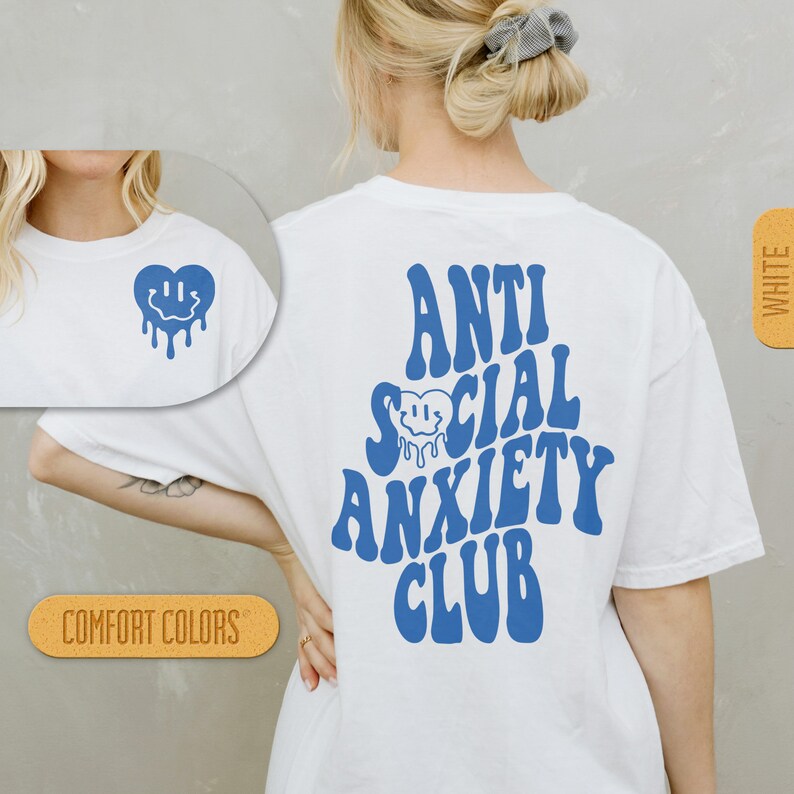 K&ouml;nnte beinhalten: Wei&szlig;es T-Shirt mit blauem Text, der "Anti Social Anxiety Club" in einer Retro-Schriftart lautet. Ein blaues, tropfendes Smiley-Gesichtsherz befindet sich im Text. Das Shirt ist in Wei&szlig; und in Komfortfarben erh&auml;ltlich.