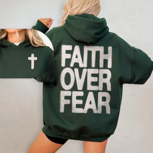 May include: A dark green hooded sweatshirt with the words "FAITH OVER FEAR" printed in white on the back. A small white cross is visible on the front of the sweatshirt.