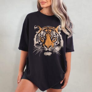 May include: Black oversized t-shirt with a vintage-style tiger face graphic printed on the front.