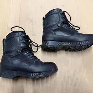 Könnte beinhalten: Ein Paar schwarze taktische Stiefel mit hohem Schaft. Die Stiefel haben einen Schnürverschluss, eine verstärkte Zehenpartie und eine robuste, strukturierte Sohle. Die Stiefel sind aus strapazierfähigen Materialien gefertigt und eignen sich für Outdoor-Aktivitäten. Ca. 25 cm lang.
