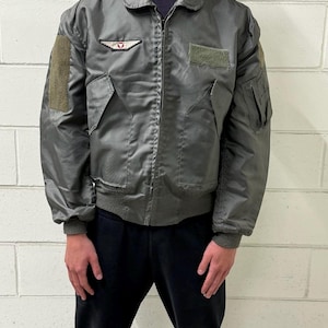 Puede incluir: Chaqueta bomber gris con cremallera, dos bolsillos delanteros y parches en las mangas y el pecho. La chaqueta tiene cuello y puños de canalé. La chaqueta está hecha de un material brillante.