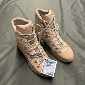 Puede incluir: Un par de botas de senderismo de cuero beige con cordones blancos. Las botas tienen una cremallera en el lateral y una etiqueta que dice "CALIDAD".