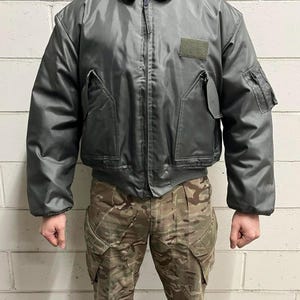 Puede incluir: Una chaqueta bomber verde oscuro con cierre de cremallera y un parche en el pecho izquierdo. La chaqueta tiene dos bolsillos en la parte delantera y uno en la manga izquierda.