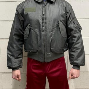 Puede incluir: Una chaqueta bomber verde oscuro con cierre de cremallera y un parche en la manga izquierda.