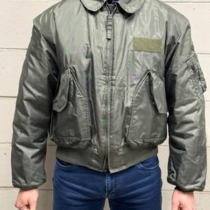 Puede incluir: Chaqueta bomber verde salvia con cremallera, dos bolsillos delanteros y un parche en el pecho. La chaqueta tiene dobladillo y puños de canalé. El modelo lleva vaqueros azules.