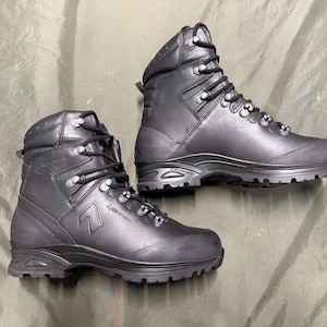 May include: A pair of black leather hiking boots. The boots have a high-top design with multiple eyelets for the laces, and a thick, rugged sole. The boots are designed for outdoor activities and provide ankle support.