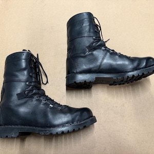 May include: Pair of black leather combat boots with high tops and rugged soles. The boots have laces and metal eyelets. The boots are designed for durability and protection.