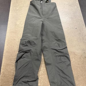 May include: Olive green bib overalls with adjustable shoulder straps and a front zipper closure. The work pants have reinforced knee patches and hook-and-loop closures at the ankles. The overalls are made of a durable, water-resistant material.