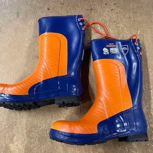 May include: A pair of orange and blue rubber work boots. The boots have a blue upper and orange lower section. The boots have a black sole and orange laces. The boots have the text "nom FORST" printed on the side.