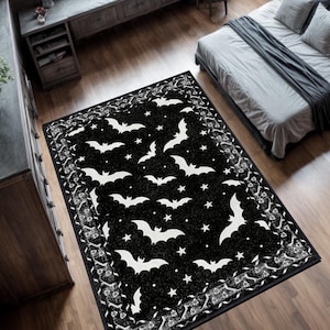 May include: A black rectangular rug featuring a pattern of white bats and stars. The rug has a decorative border with floral and scroll designs. The rug is placed on a wooden floor in a bedroom setting.