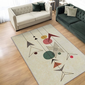 Può includere: Un tappeto rettangolare con sfondo color crema caratterizzato da un motivo geometrico di sottili linee nere, frecce stilizzate e cerchi pieni nei toni del rosso, giallo, verde e marrone, rifinito con un semplice bordo grigio.