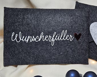 Könnte beinhalten: Zwei dunkelgraue Filztaschen, eine rechteckige mit dem Wort "Wunscherfüller" in weißer Schrift und einem kleinen roten Herz, und eine Umschlagförmige mit einem grauen Herzverschluss. Zwei blaue Weihnachtskugeln im Vordergrund.