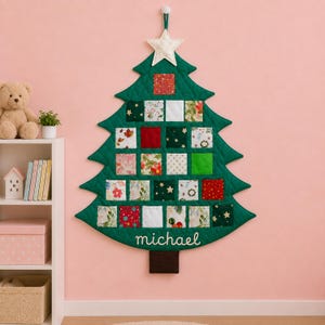 May include: A quilted fabric Christmas tree wall hanging featuring twenty-four small square pockets with various holiday-themed patterns in red, green, white, and gold. The tree is topped with a white star and displays the name michael in white.