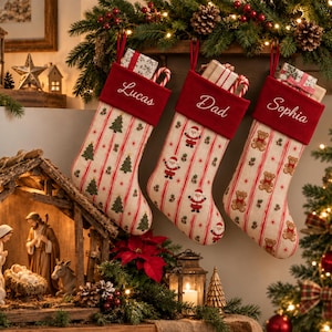 May include: Three Christmas stockings with red velvet cuffs featuring the embroidered names Lucas, Dad, and Sophia. The stockings have a cream-colored fabric body with vertical red stripes, green pine tree patterns, Santa Claus figures, and teddy bears.