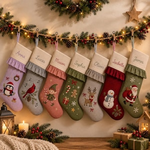 May include: Seven personalised Christmas stockings hanging in a row, each featuring a unique embroidered character including a penguin, cardinal, elf, gingerbread man, reindeer, snowman, and Santa Claus, with names Anna, Lucas, Mason, Sophia, Oliver, Isabella, and James.
