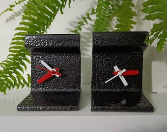 May include: Two black metal bookends shaped like a railroad track with a clock face on each. The clock hands are red and white.