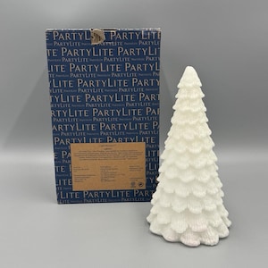 May include: A white, textured, Christmas tree-shaped candle with a layered design. The candle is next to a box with the text "PARTYLITE" in a repeating pattern. The box is blue and white.