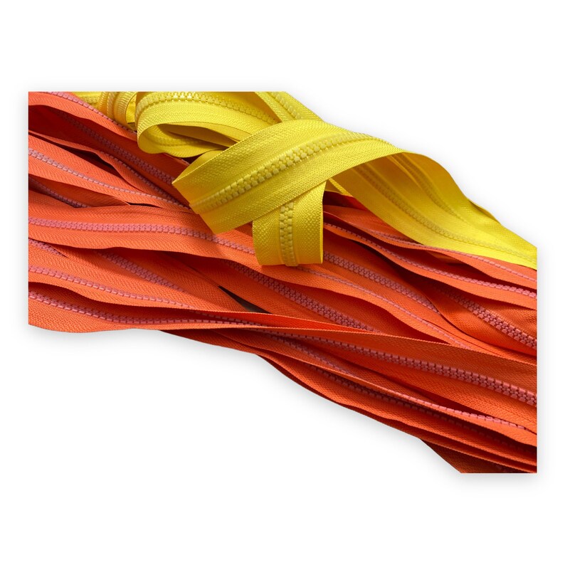 Op de afbeelding: Een close-up van twee ritsbanden, een oranje en een gele. De banden zijn gemaakt van nylon en hebben een gladde afwerking. De ritsen zijn ideaal voor naaiprojecten.