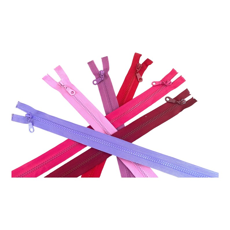 Op de afbeelding: Assortiment van kleurrijke ritsen in verschillende tinten roze, rood en paars. De ritsen zijn in een stervorm gerangschikt.