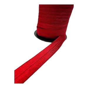 Può includere: Un rotolo di nastro elastico rosso. Il nastro è avvolto attorno a un rotolo nero e ha una larghezza di circa 2,5 cm.