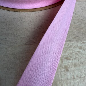 May include: A close-up of a pink cotton bias tape, a type of fabric trim used for finishing edges of fabric.