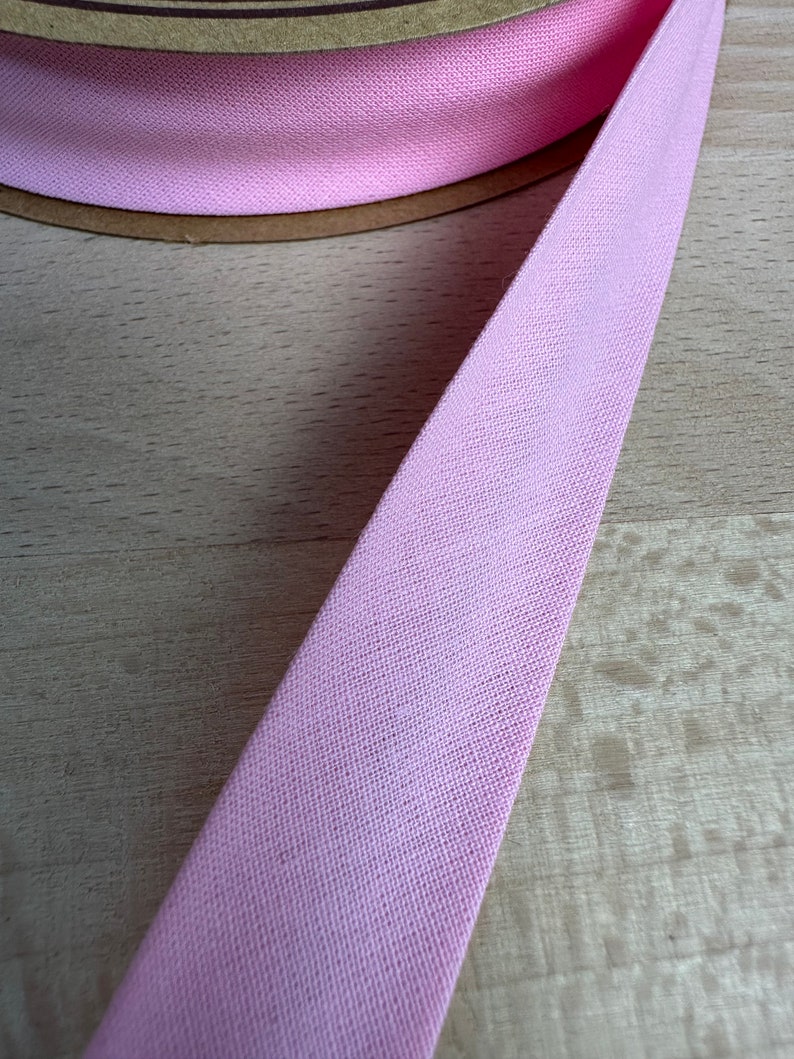May include: A close-up of a pink cotton bias tape, a type of fabric trim used for finishing edges of fabric.
