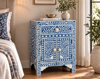 May include: A rectangular bedside table featuring a vibrant blue and white floral inlay pattern. The piece includes one top drawer and two lower cabinet doors, each equipped with round white knobs. The design is consistent across all visible sides.