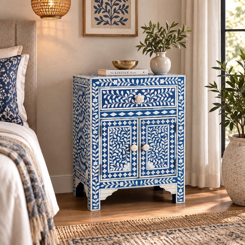 May include: A rectangular bedside table featuring a vibrant blue and white floral inlay pattern. The piece includes one top drawer and two lower cabinet doors, each equipped with round white knobs. The design is consistent across all visible sides.