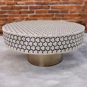 May include: A round coffee table with a white and black geometric pattern on the top. The table has a silver metal base.