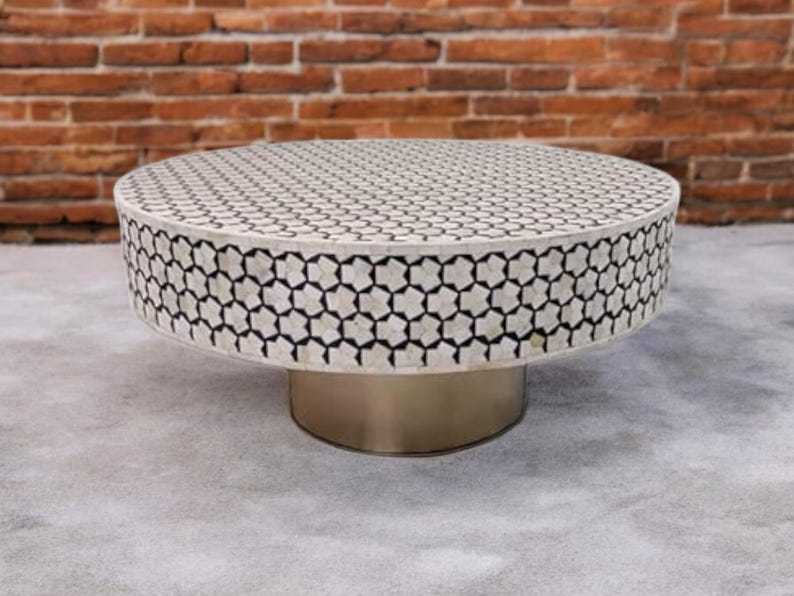 May include: A round coffee table with a white and black geometric pattern on the top. The table has a silver metal base.