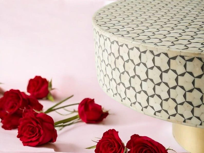 May include: A white round table with a black geometric pattern. The table is made of bone inlay and has a gold base. The table is surrounded by red roses.
