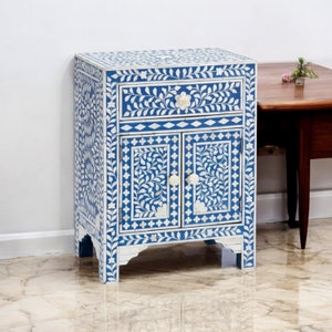 May include: A rectangular cabinet featuring a vibrant blue and white floral inlay pattern. The piece includes one top drawer and two lower doors, each adorned with small, round, off-white knobs. The exterior is covered in intricate leaf motifs.