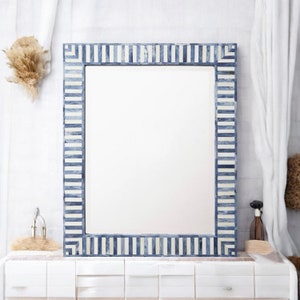 Op de afbeelding: Rechthoekige spiegel met een blauw-wit gestreepte lijst. De spiegel staat op een witte kast. De lijst heeft een patroon van afwisselend blauwe en witte rechthoekige tegels.