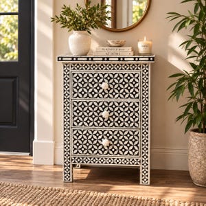 May include: A rectangular three-drawer chest featuring a black and white geometric floral pattern across the front and sides. The chest has three white, flower-shaped knobs and a flat top surface. The frame is constructed with a repeating circular motif.